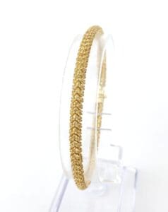 Gold bangle displayed on a clear stand.