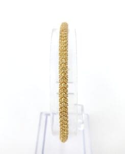 Gold bangle on a clear stand.