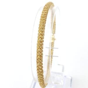 Gold bangle displayed on a clear stand.