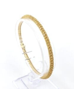 Gold bracelet on a clear display stand.