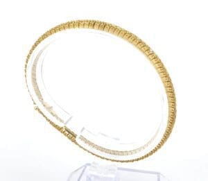Gold bracelet on a clear display stand.