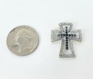 Quarter beside jeweled cross pendant on white background.
