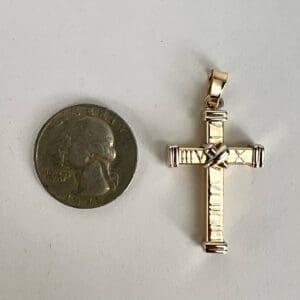 Gold cross pendant beside a quarter coin.