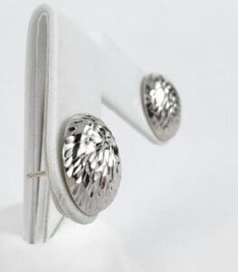 Silver textured earrings on white display stand.