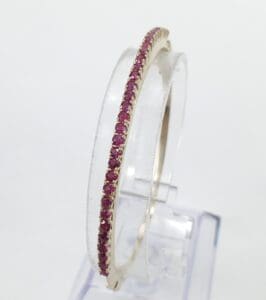 Gold bangle with pink gemstones displayed upright.
