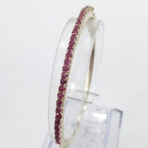 Gold bangle with pink gemstones displayed upright.