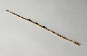 Gold bracelet with dark gemstones on white.