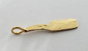 Gold cricket bat-shaped pendant on white background.