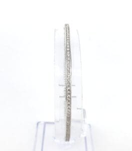 Diamond-studded silver bangle on clear stand.