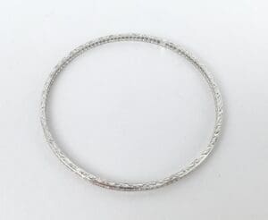 Silver bangle with engraved pattern on surface.