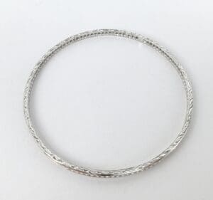 Silver bangle with intricate design on white background.