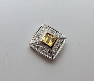 Square diamond brooch with yellow gemstone center.