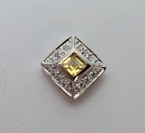 Square diamond brooch with yellow gem.