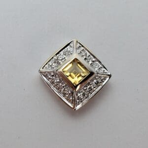 Square diamond brooch with yellow gem.
