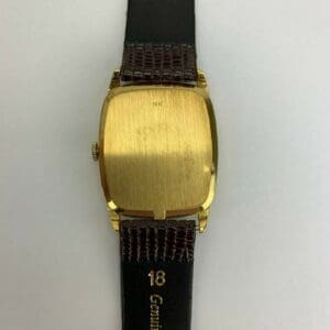 Gold watch back with black leather strap.