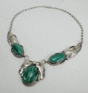 Silver necklace with green gemstones and feathers.