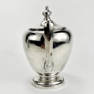 Silver teapot with ornate handle and lid.