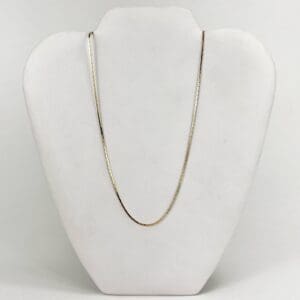 Gold chain on a white display stand.
