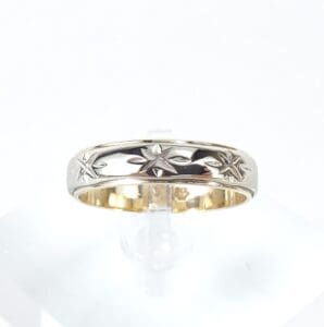 Silver ring with star engravings on stand.
