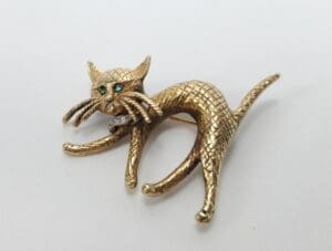 Gold cat brooch with green gemstone eyes.