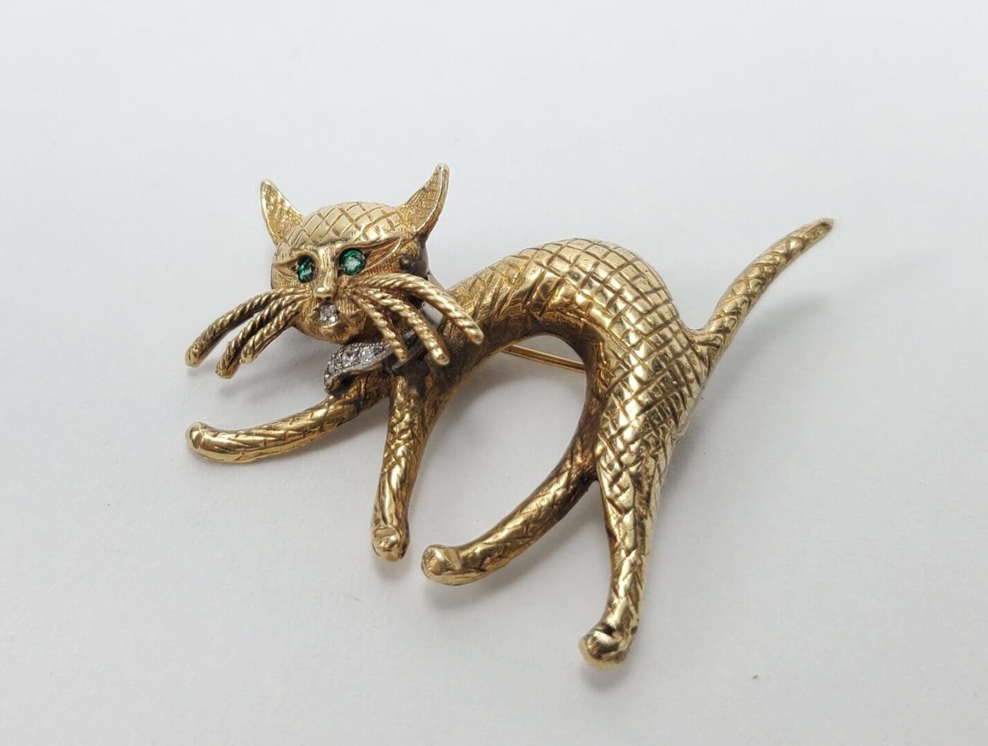 Gold cat brooch with green gemstone eyes.