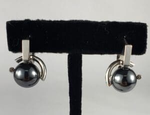 Silver and black earrings on display stand.