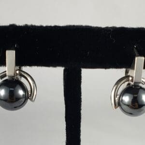 Silver and black earrings on display stand.