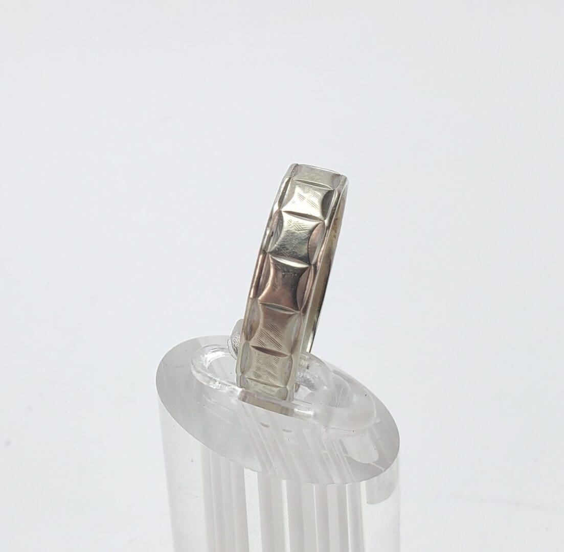 Silver ring with geometric pattern on stand.