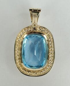 Gold pendant with blue gemstone centerpiece.