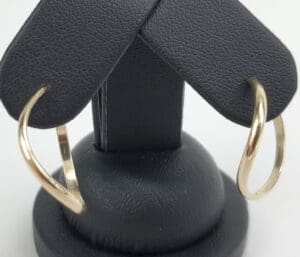 Gold hoop earrings on black display stand.
