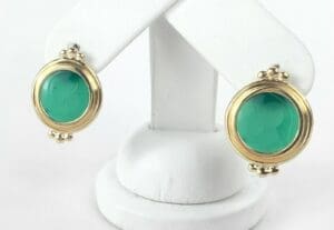 Gold and green round earrings on stand.
