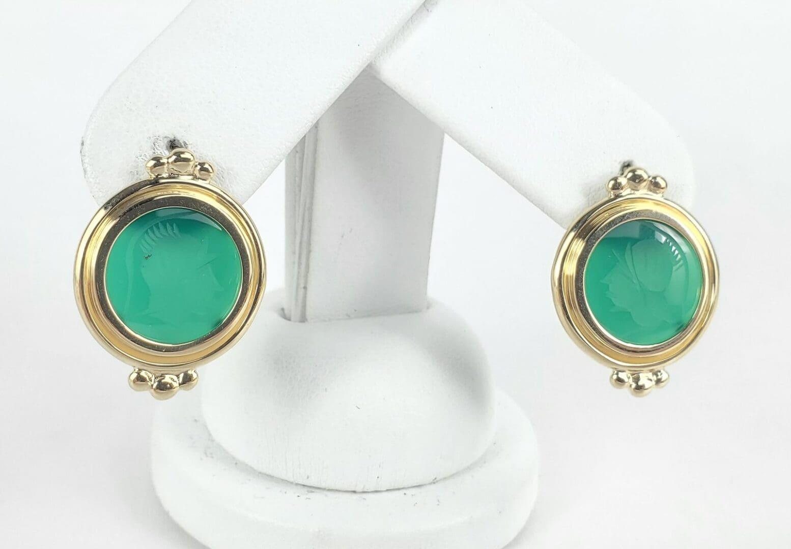 Gold-framed green cameo earrings on display.