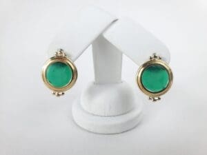 Gold earrings with green stone on display.