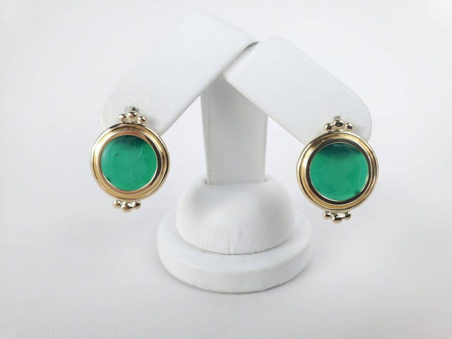 Gold earrings with green stone on display.