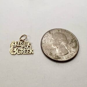 Charm reading "Kiss Me I'm Greek" beside quarter.