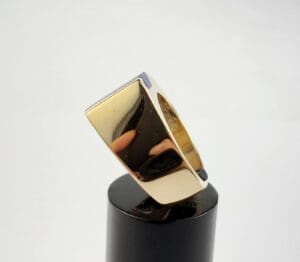Gold rectangular ring on black stand.