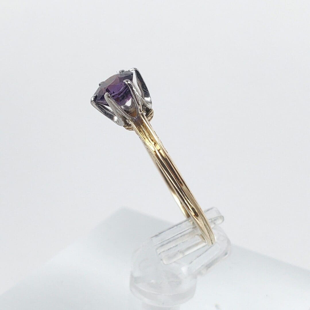Gold ring with purple gemstone on stand.