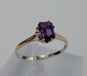 Gold ring with rectangular purple gemstone.