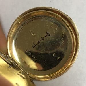 Engraved gold watch case interior with writing.