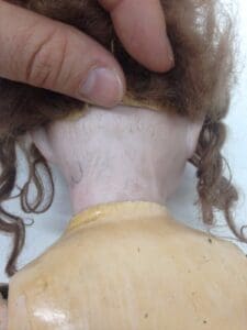 Hand holding doll's head with visible markings.