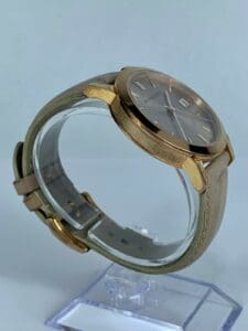 Gold watch with leather strap on stand.