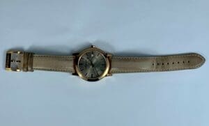 Gold wristwatch with a beige strap.