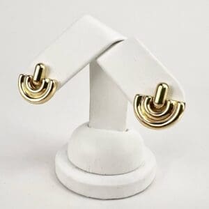 Gold geometric earrings on white display stand.