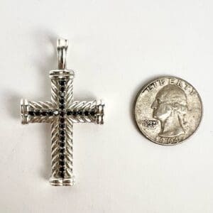 Silver cross pendant next to a quarter.