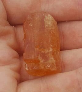 Hand holding an orange crystal mineral specimen.