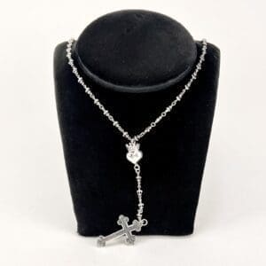 Silver rosary necklace on black display stand.