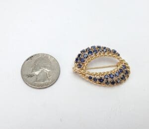 Gold brooch with blue stones, quarter nearby.