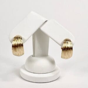 Gold textured hoop earrings on display stand.