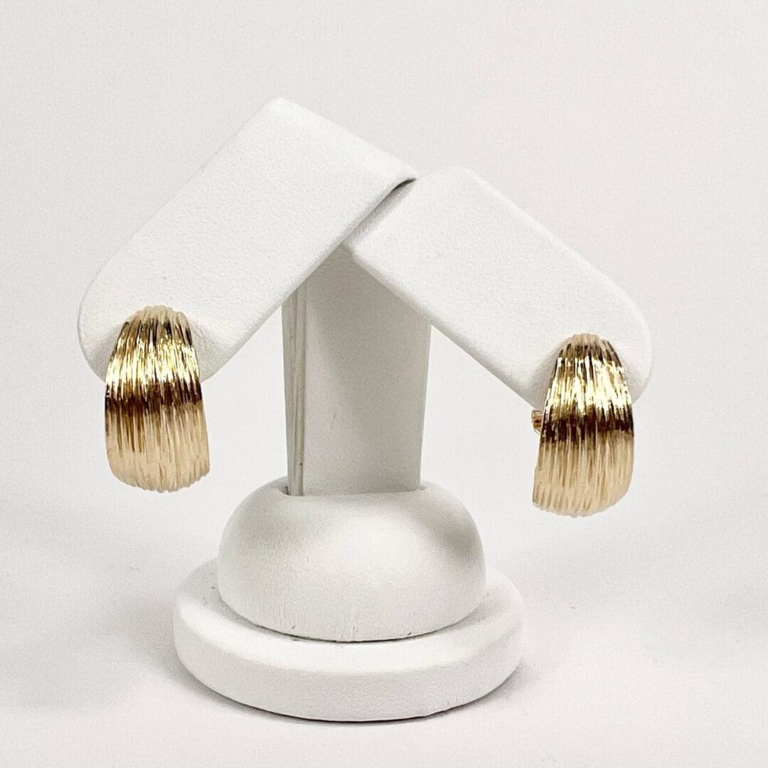 Gold textured hoop earrings on display stand.