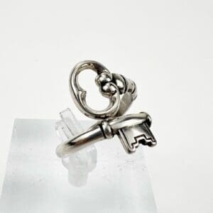 Silver ring with key design on stand.